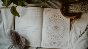 Atvērta grāmata ar astroloģiskiem simboliem uz gultas blakus istabas augam.