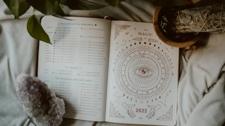 Atvērta grāmata ar astroloģiskiem simboliem uz gultas blakus istabas augam.