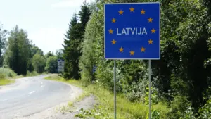 Zila ceļa zīme ar uzrakstu Latvija uz ceļa fona Latvijas laukos.
