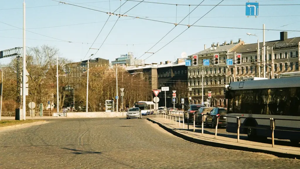 Iela Rīgā ar sabiedrisko transportu un automašīnām saulainā dienā.