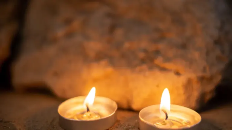 Divas degošas tējas sveces uz smilšainas virsmas ar neasu akmeni fonā krēslā.