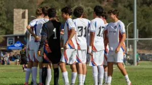 Jaunie futbolisti sapulcējušies uz apspriedi laukuma malā pirms svarīgas futbola spēles sākuma.
