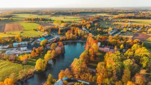 Grezns rudens skats uz Latvijas upi un krastā esošo mazpilsētu no putna lidojuma.