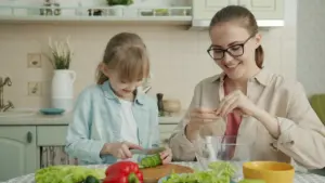 Māte kopā ar meitu gatavo veselīgas pusdienas mājās pirms skolas gaitām.