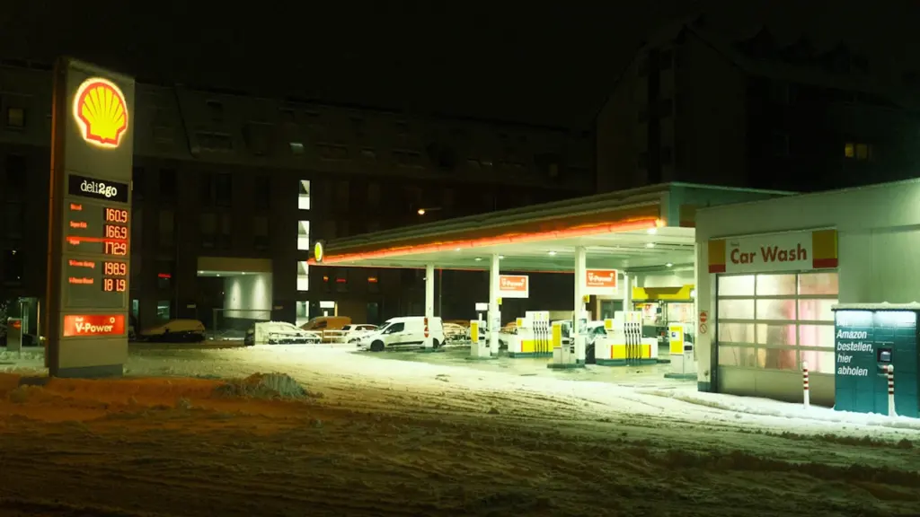Degvielas uzpildes stacija vakarā ar sniegu, ilustrējot ikdienas izdevumus autovadītājiem Latvijas ziemas apstākļos.