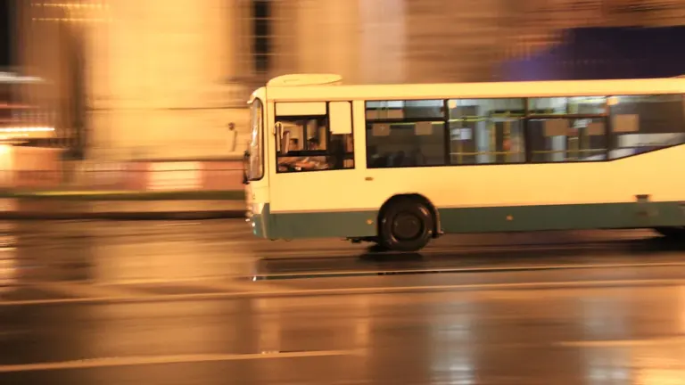 Steidzīgā tempā braucošs autobuss pa pilsētas ielām tumšajā diennakts laikā
